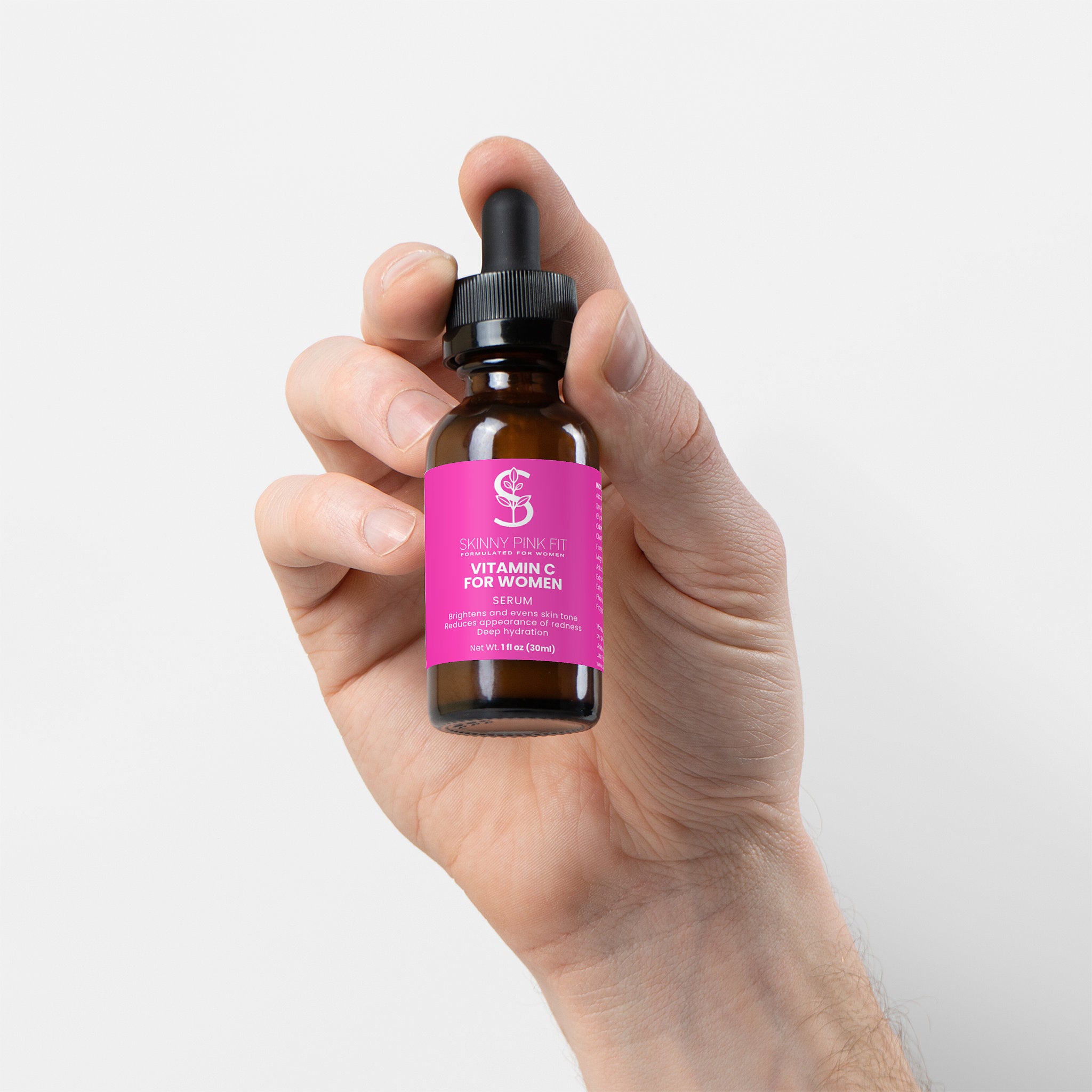 Hand holding a bottle of vitamin C serum for women against a white Skinny Pink Fit