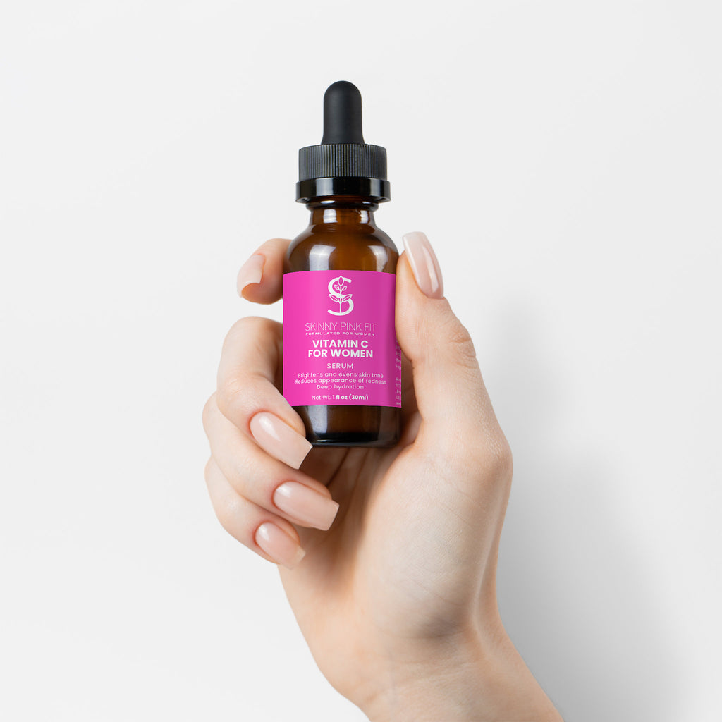 Hand holding a bottle of vitamin C serum with a pink label against a white background, Skinny Pink Fit